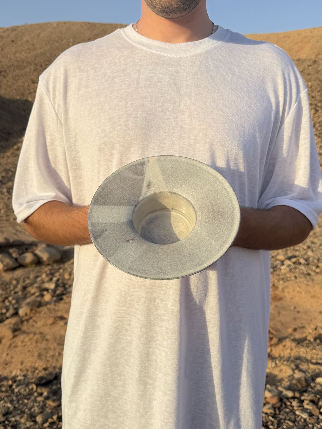 Wide grey ceramic bowl held against a white t-shirt, desert background