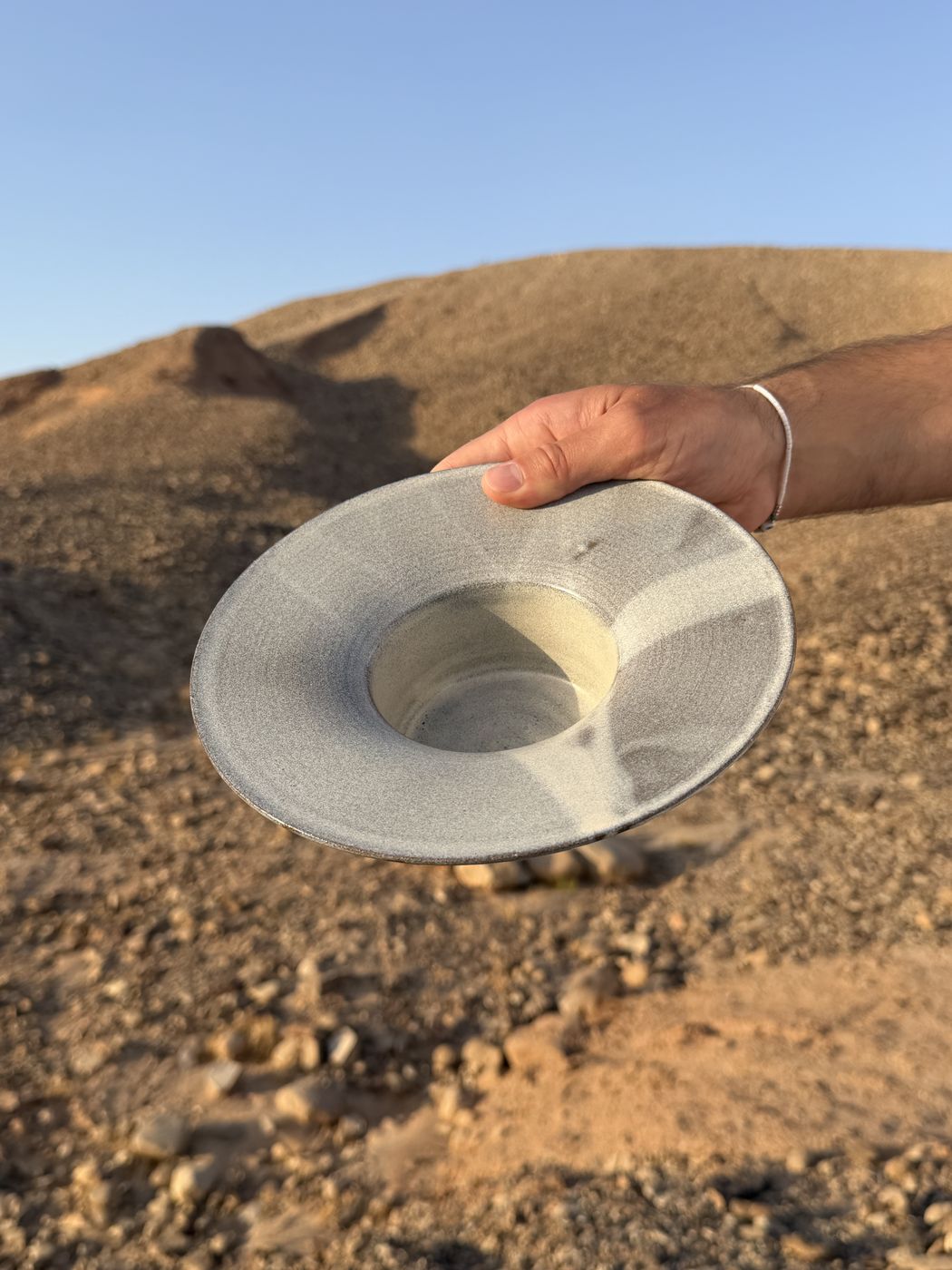 Grey ceramic bowl held up against a desert sky
