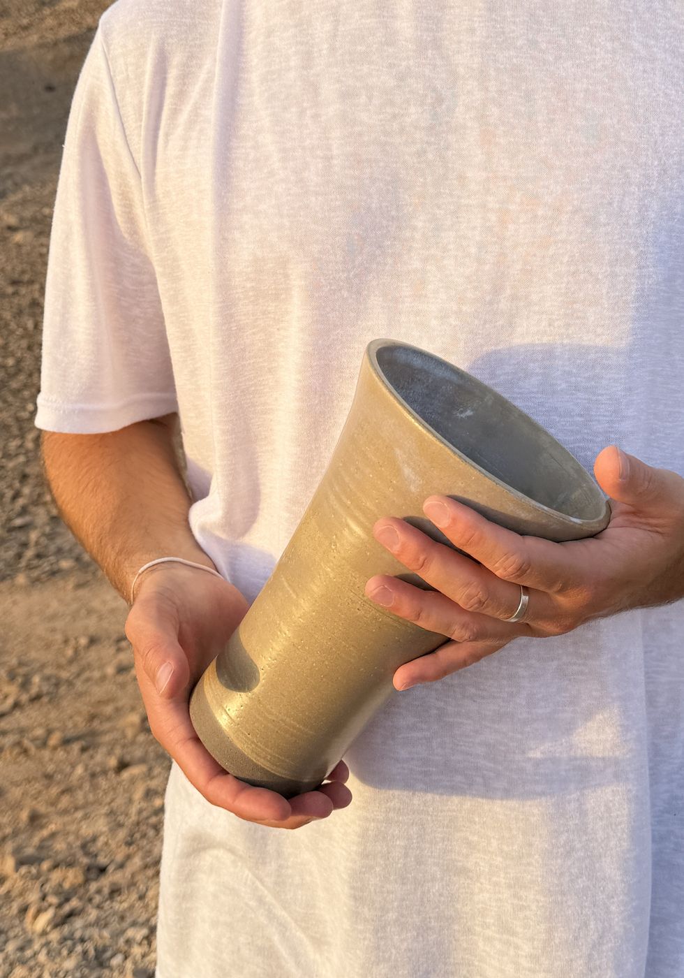 Tall speckled ceramic cup held in two hands, desert background